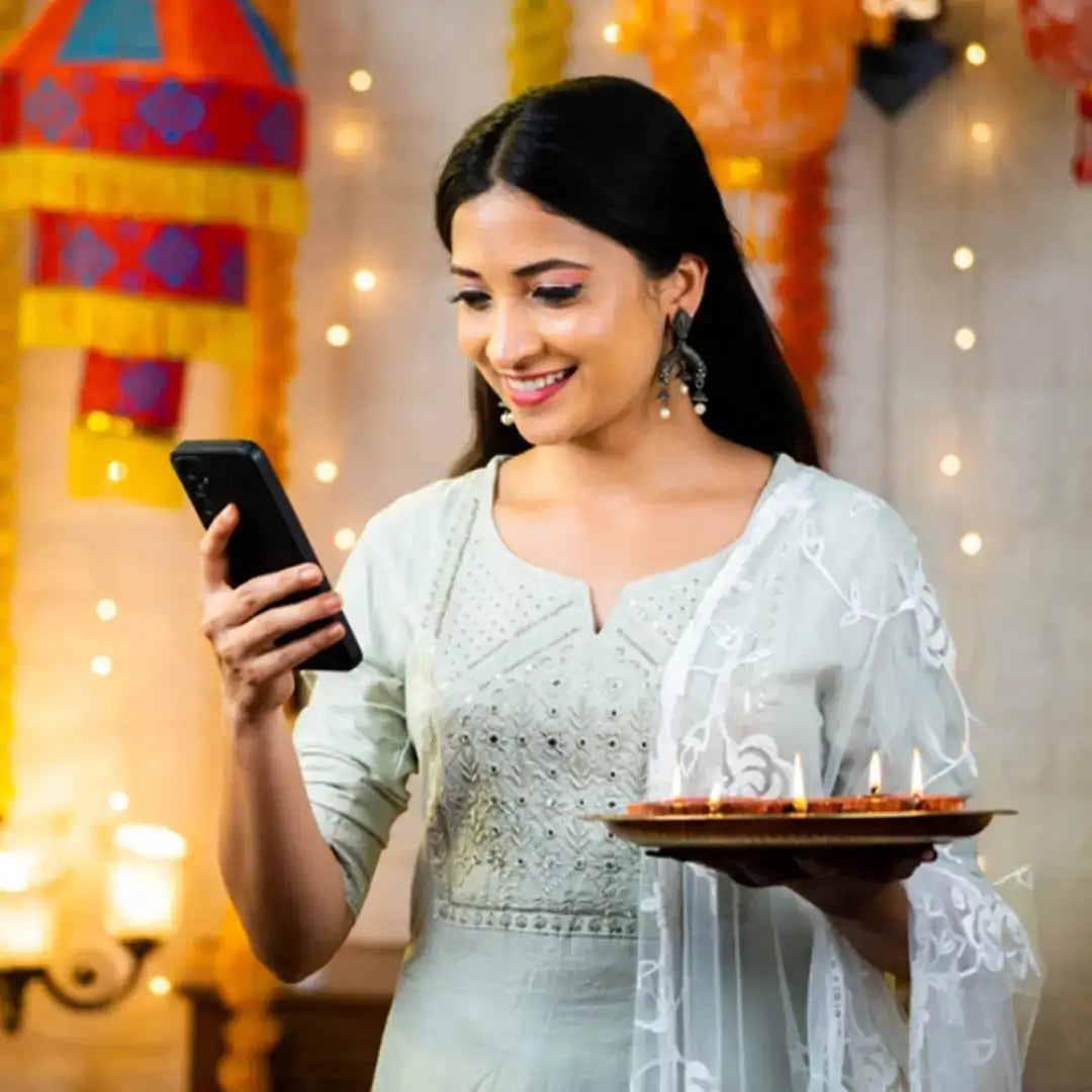 Woman in traditional Indian attire with intricate designs, enjoying Indian celebrations on smartphone.