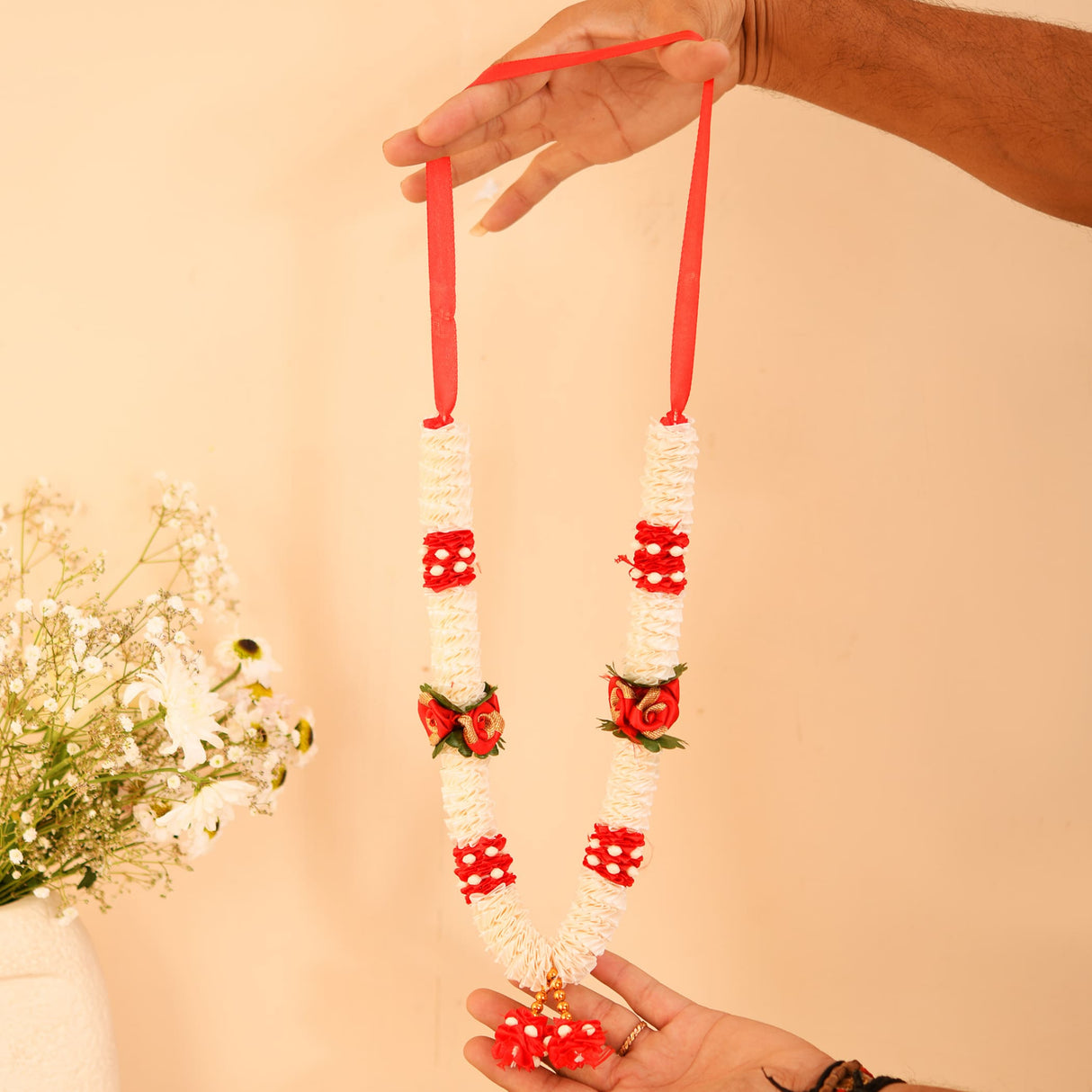 Red white floral idol mala garland with rose accents, held by hands