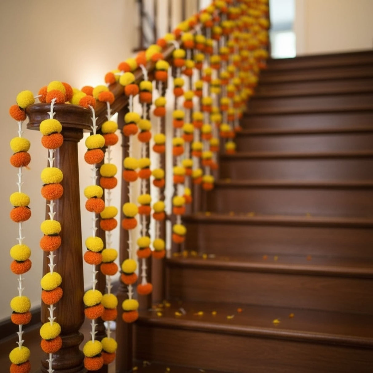 Orange and yellow pompom garlands strung along a wooden staircase railing for festive decor