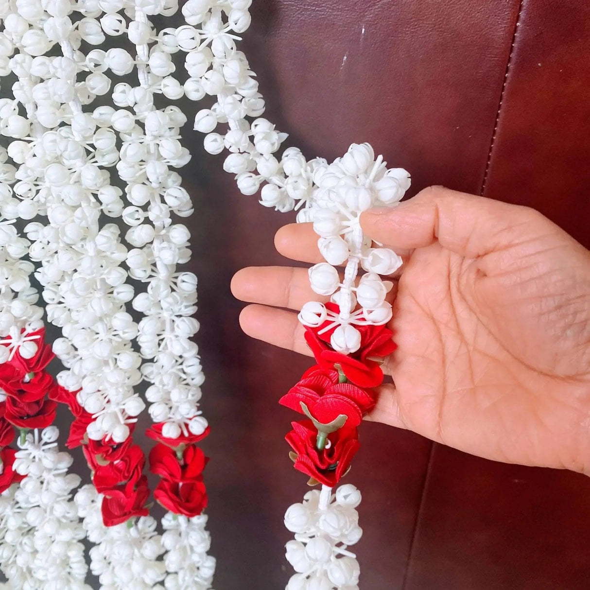 A hand holds an artificial jasmine buds and rose garland with white and red flowers for pooja and festive decor