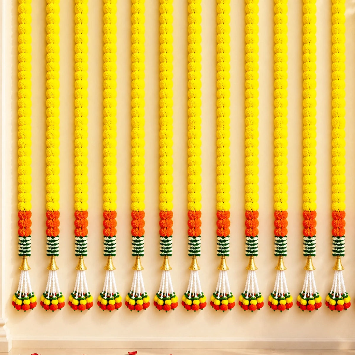 Artificial marigold garland with vibrant yellow and orange flowers, green striped accents, and gold tassels for festive decor