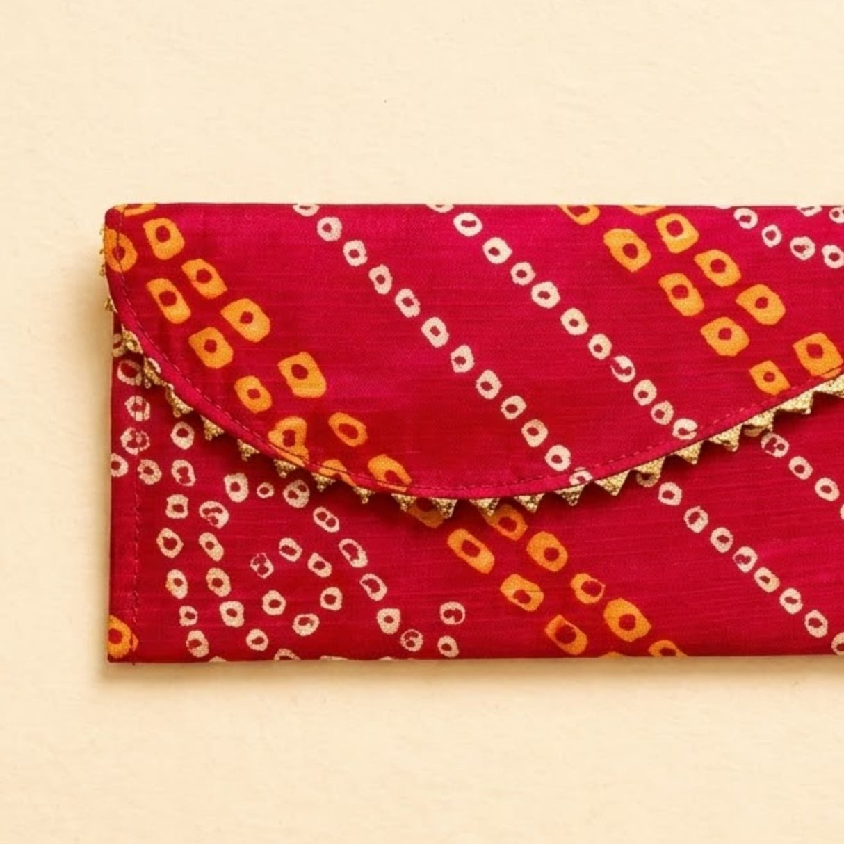 A vibrant red brocade fabric money envelope with bold orange white geometric pattern and gold scalloped trim for Indian weddings