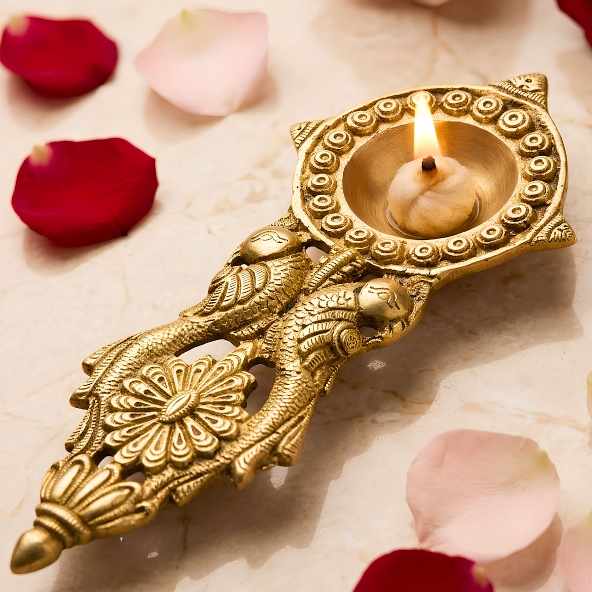 Golden brass diya with intricate peacock and floral designs featuring a lit candle for diwali pooja and aarti use