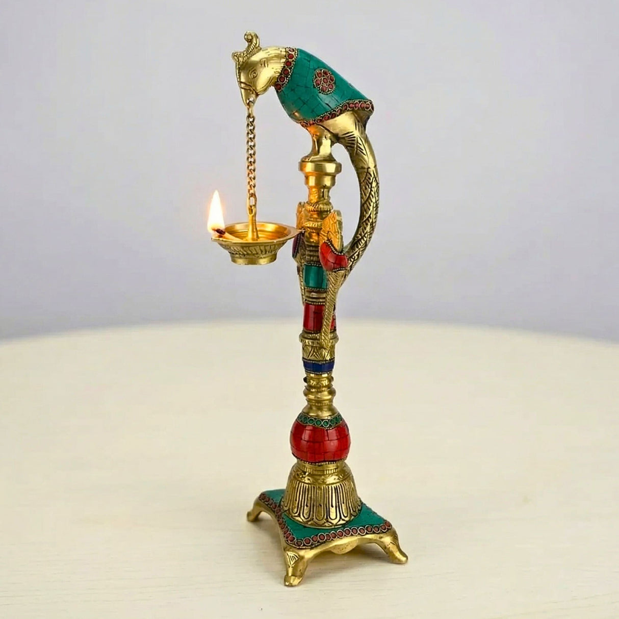 A golden brass elephant oil lamp diya with intricate engravings turquoise and red accents lit wick for temple decor