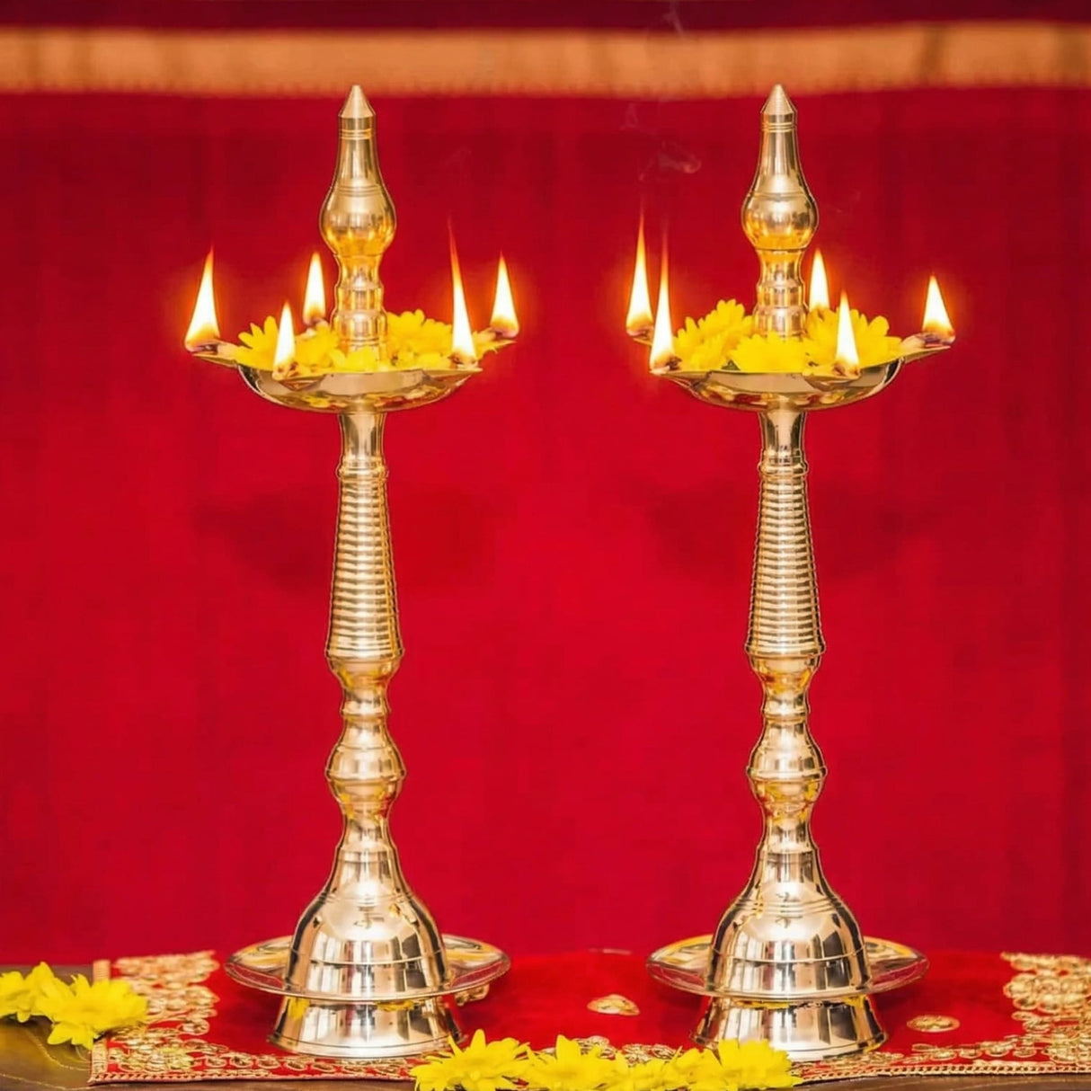 Two ornate golden brass oil lamps diya samai deepak with multiple lit candles and yellow flowers for diwali decoration