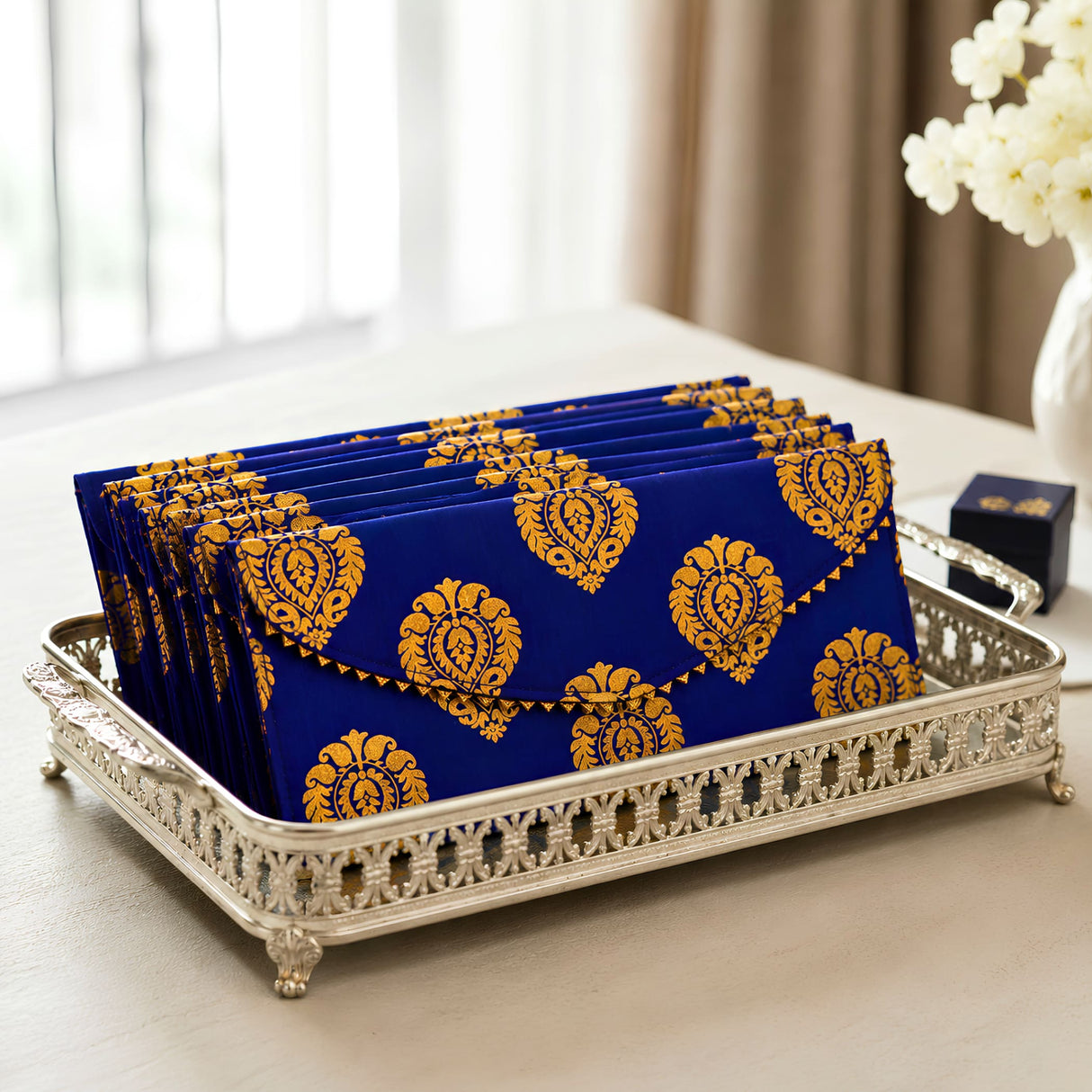 Blue and gold brocade fabric money envelopes with floral pattern arranged neatly in a silver ornate tray for gifting