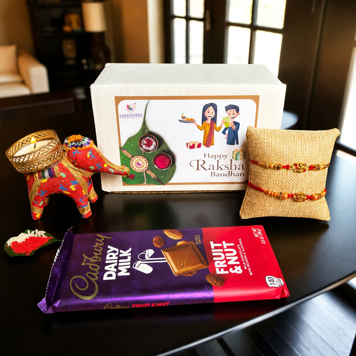 A vibrant red and gold handmade elephant-shaped candle holder with intricate gold detailing in designer rakhi gift hamper