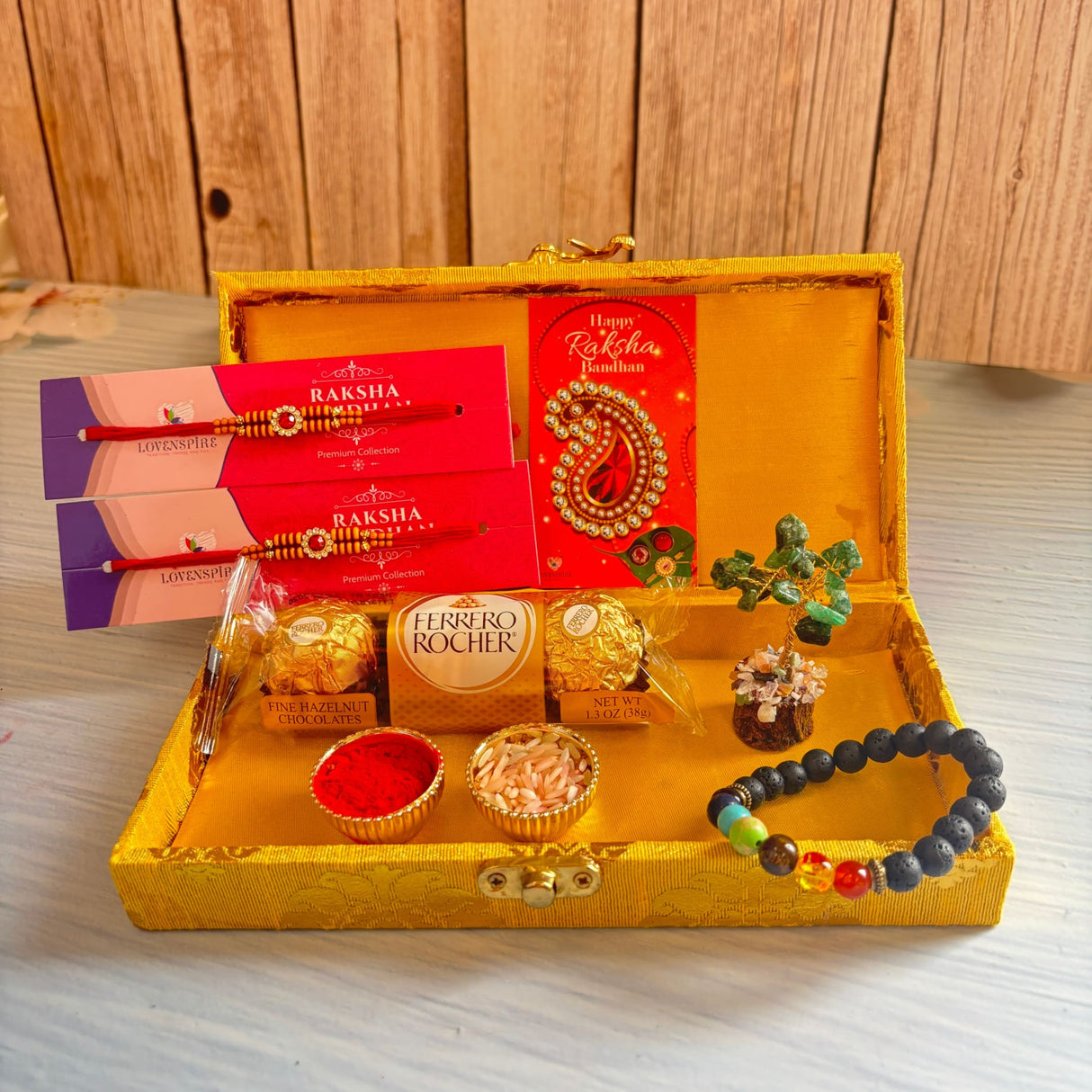 Golden ornate designer rakhi gift hamper for brother and bhabhi with red and gold rakhis, chocolates, crystal tree, and festive accessories