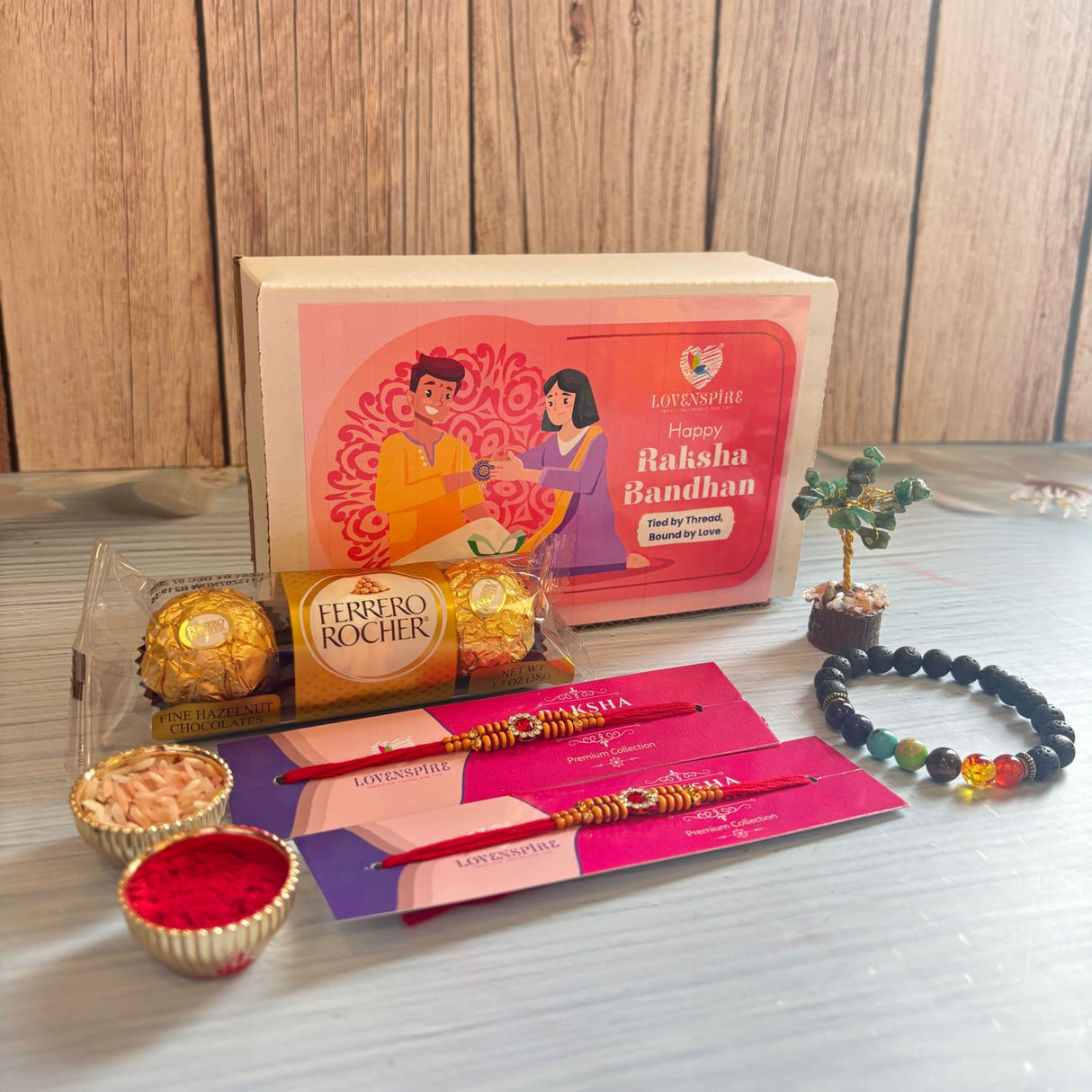 Designer rakhi gift hamper with pink and purple lovespire gift box featuring an illustration of two people exchanging gifts