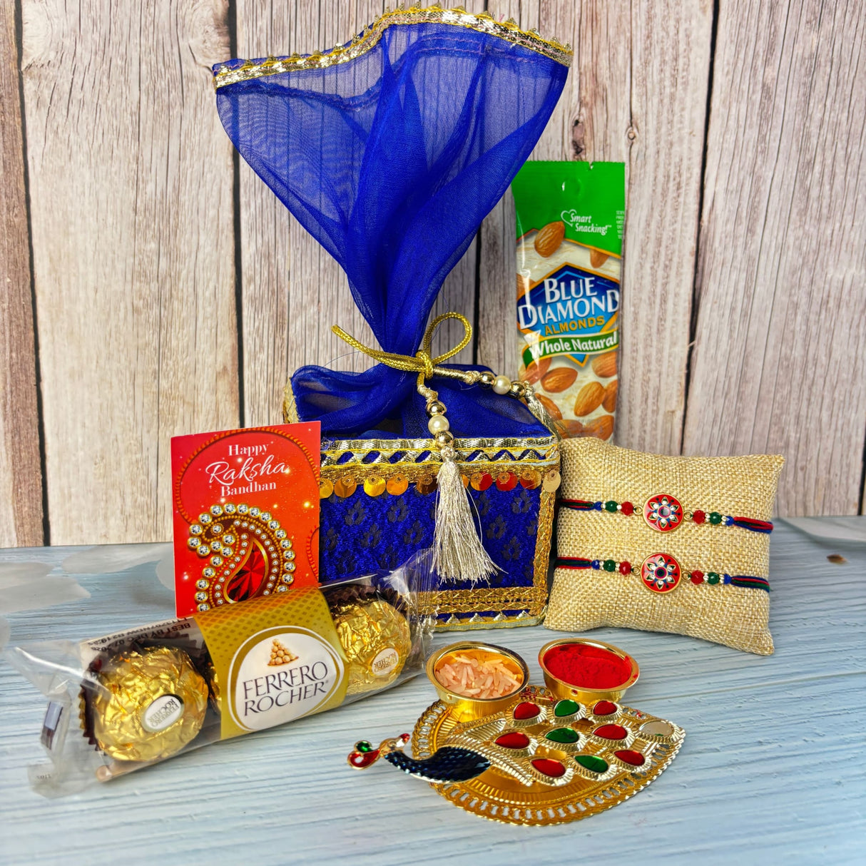Designer rakhi gift hamper set featuring a blue and gold decorative gift box with sheer blue organza and golden ribbon