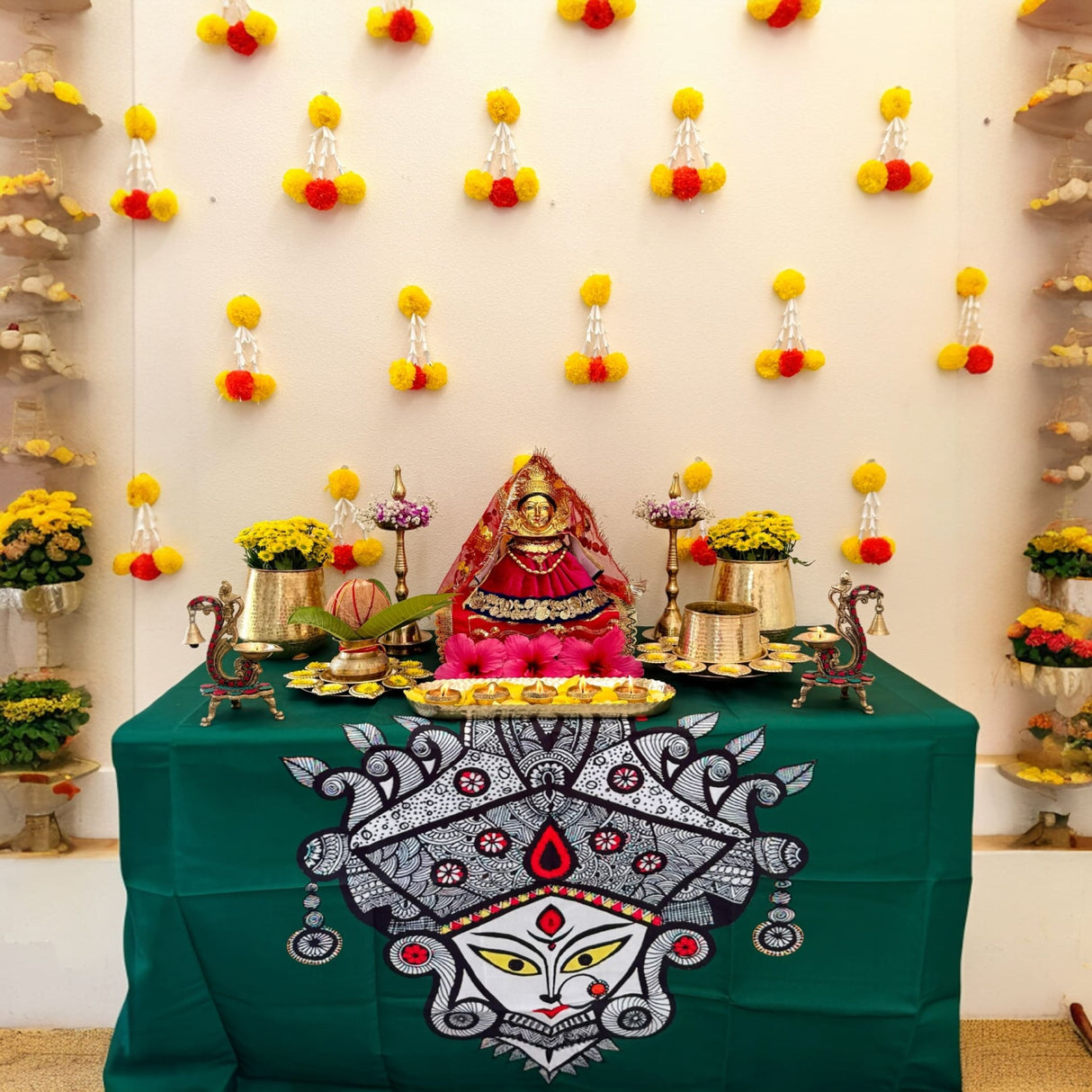 Hindu deity idol with red and gold adornments on green cloth with offerings for Diwali or wedding celebration