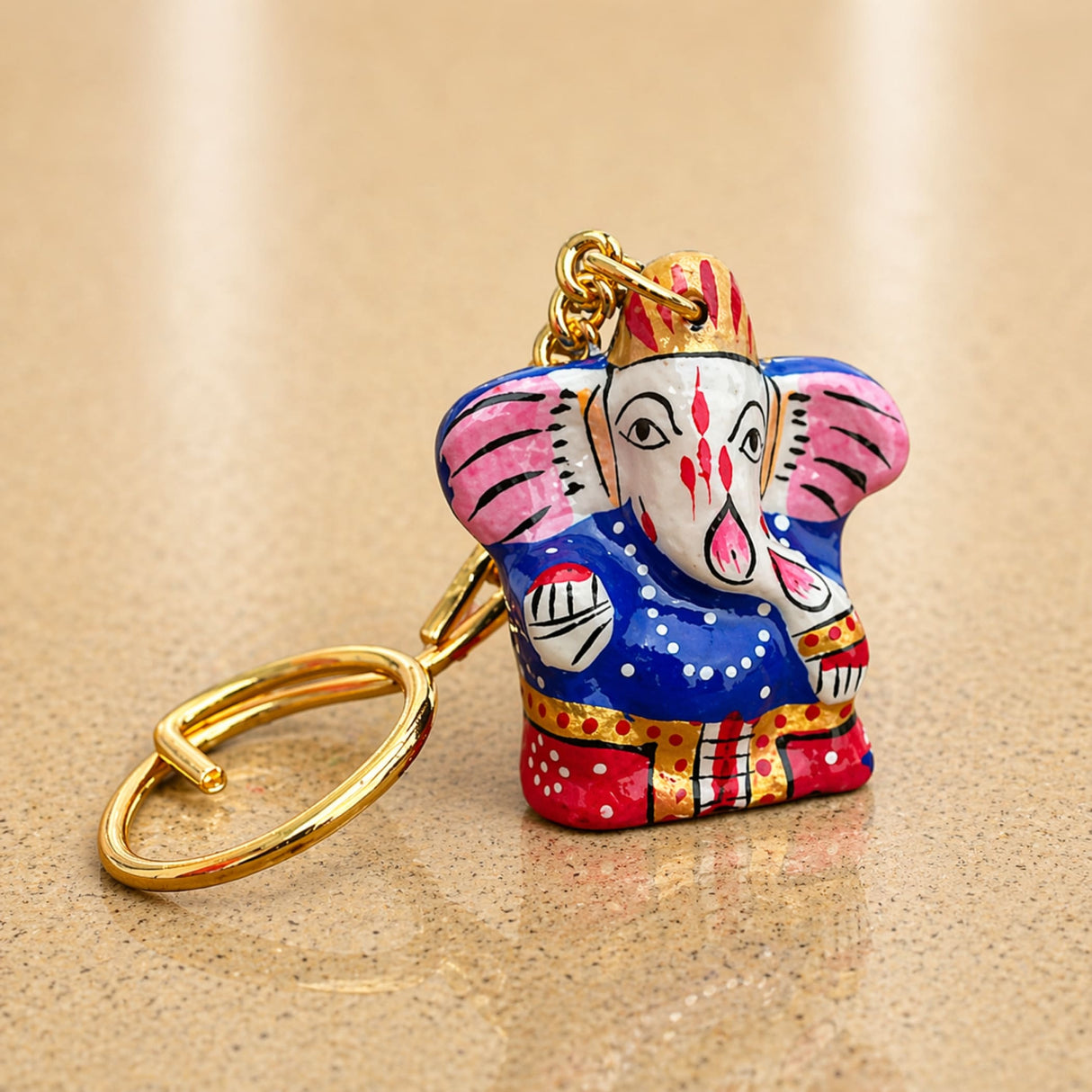 A vibrantly painted handmade ceramic Ganesha keychain with pink blue red and gold accents for return gifts and bags