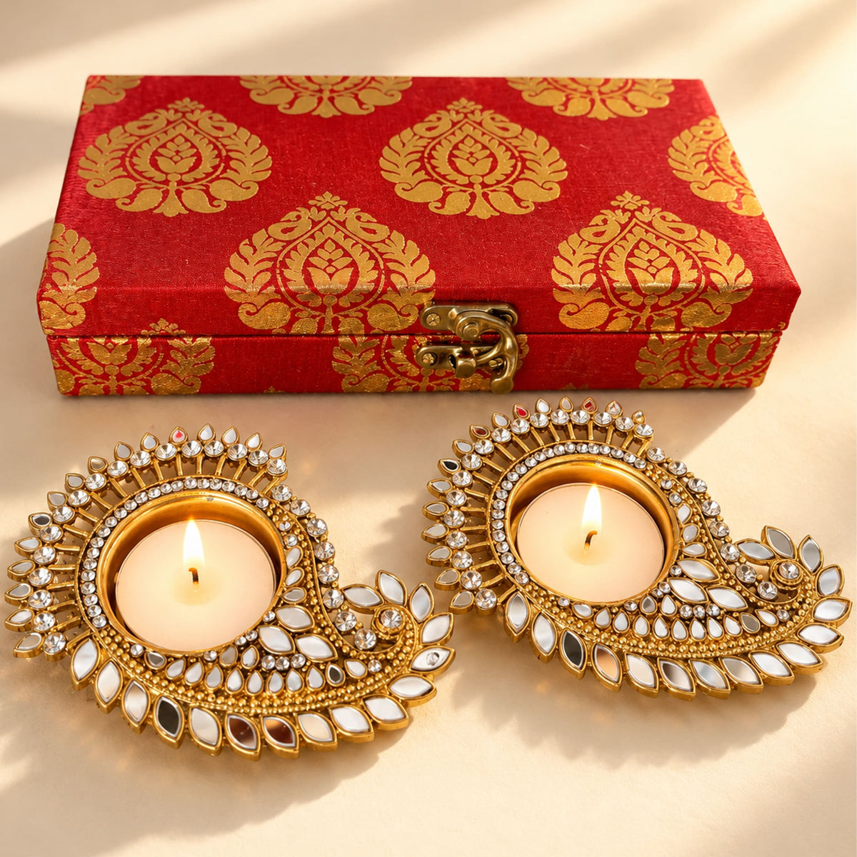 Gold-plated diya holders with mirrored and crystal embellishments holding lit candles in a traditional indian festive gift set