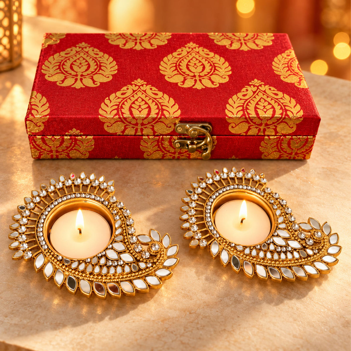 Two ornate gold-plated diya candle holders with intricate mirror and crystal paisley design in diwali gift hamper set