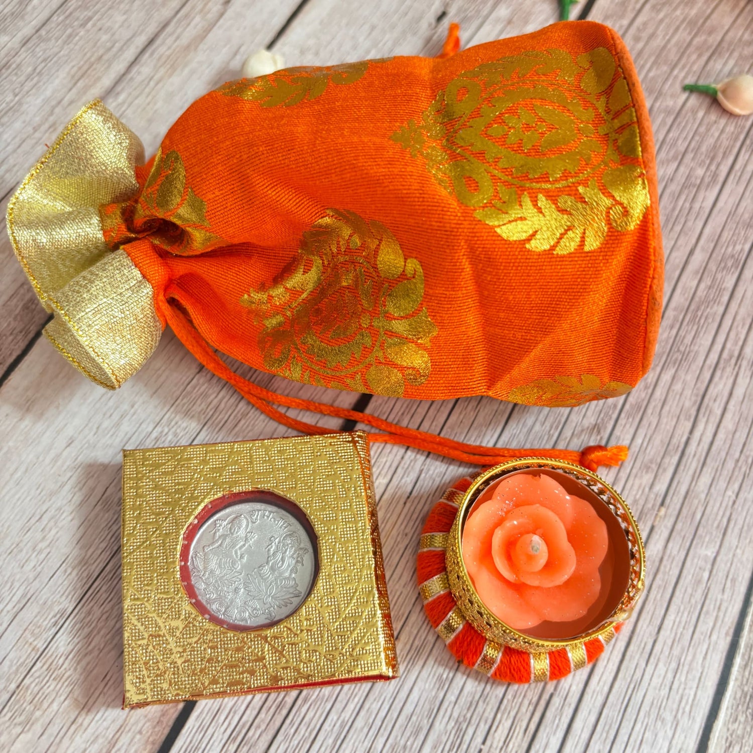 Orange brocade potli bag with silver coin and flower-shaped candle for Diwali gifting