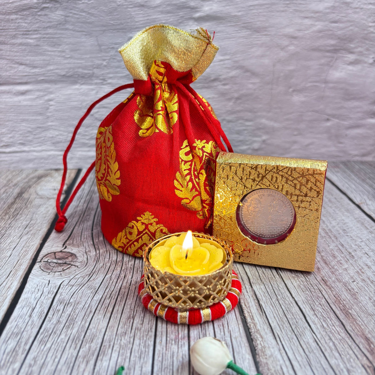 Red and gold fabric drawstring pouch with lit yellow flower-shaped candle in gold holder