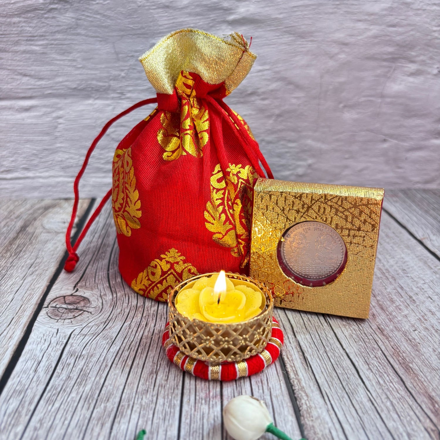 Red and gold fabric drawstring pouch with lit yellow flower-shaped candle in gold holder