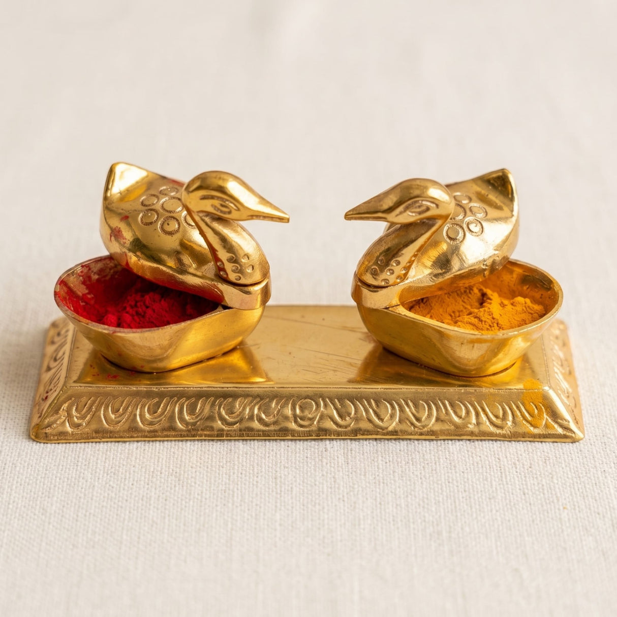 Double duck golden chopra brass spice holders with intricate patterns containing red and orange-yellow powders for pooja decor