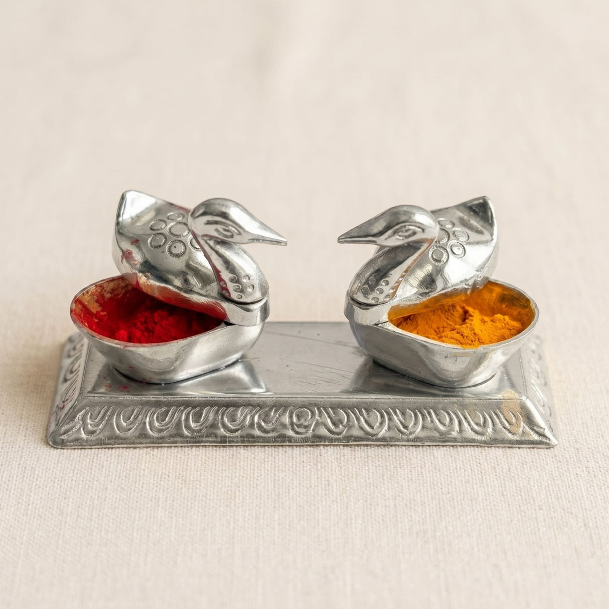 Silver duck-shaped spice holders with intricate detailing containing red and orange powders for diwali pooja decor