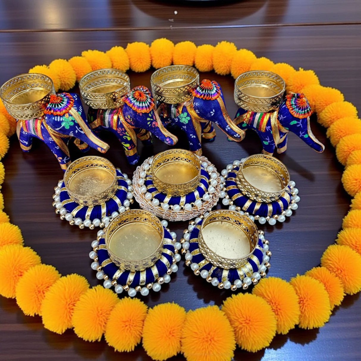 Decorative elephant-shaped and pearl-embellished candle holders within a marigold garland