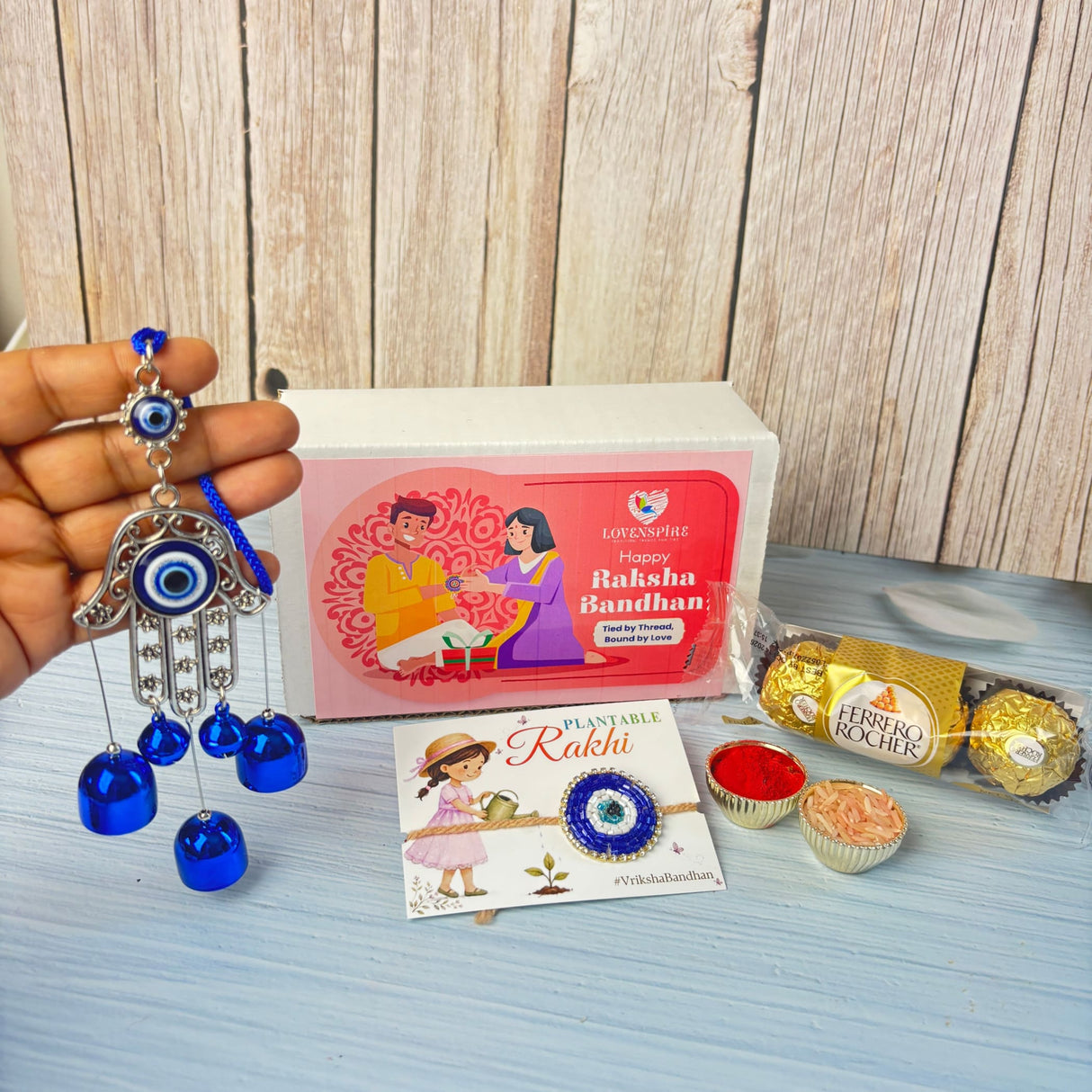 Silver hamsa hand evil eye charm with blue glass eyes and dangling blue bells in brother rakhi gift hamper