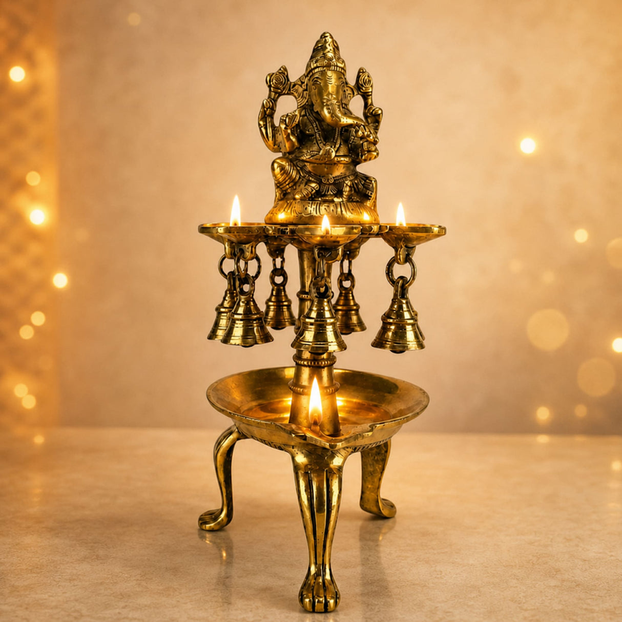 Golden brass ganesha idol atop a tiered brass oil diya lamp with hanging bells and three candle holders for pooja decor