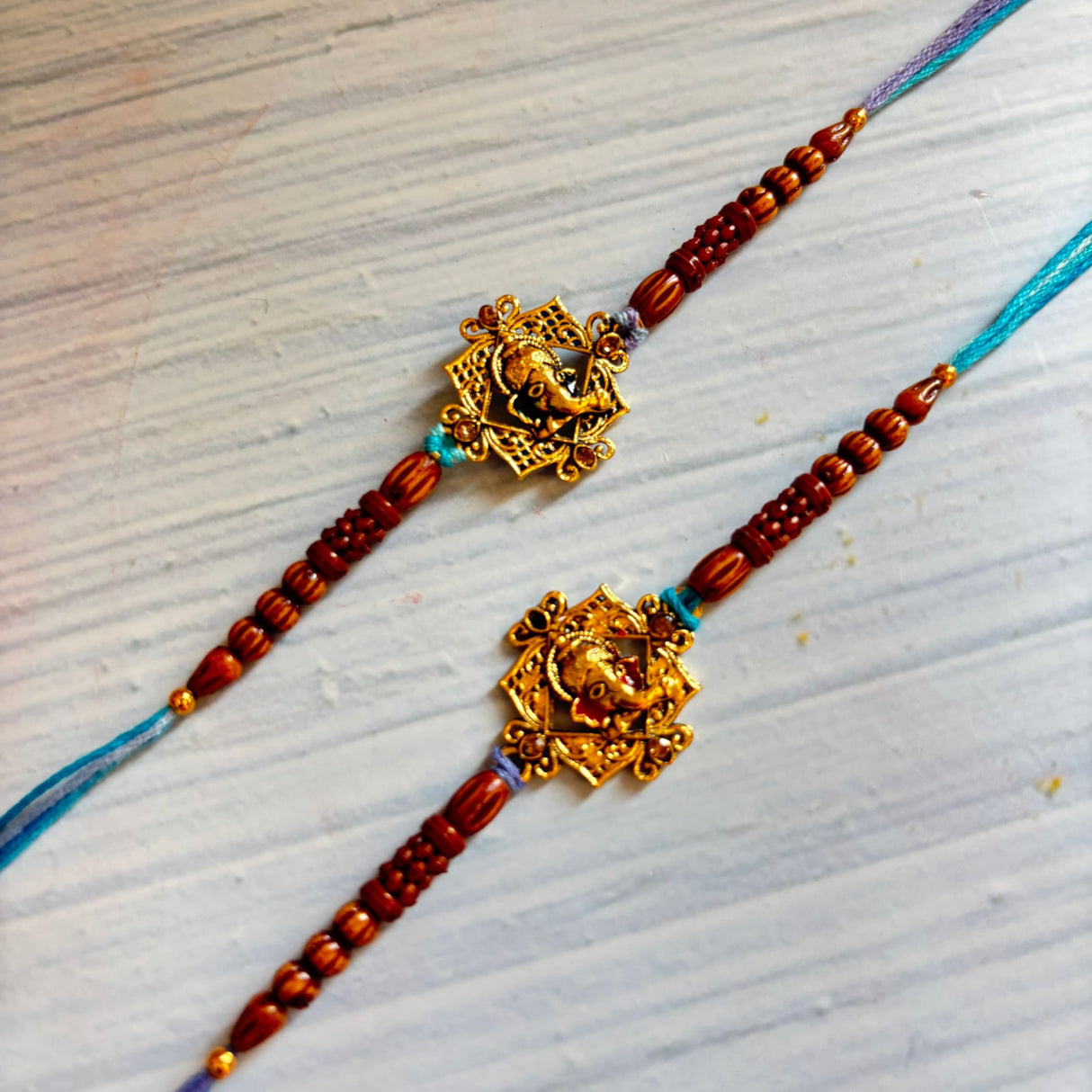 Designer ganesha rakhi featuring golden elephant charms on red beaded bracelets with blue and purple thread ends