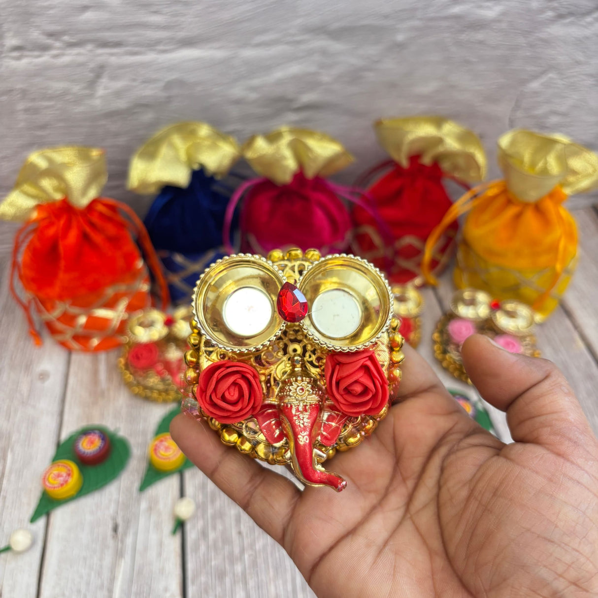 Gold-colored Ganesha-themed diya holder with two candle cups and red rose accents