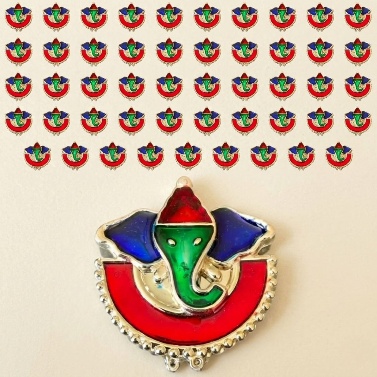 A vibrant enamel-coated Ganesha brooch with green face blue ears and red crown on silver metal base for Indian festivals