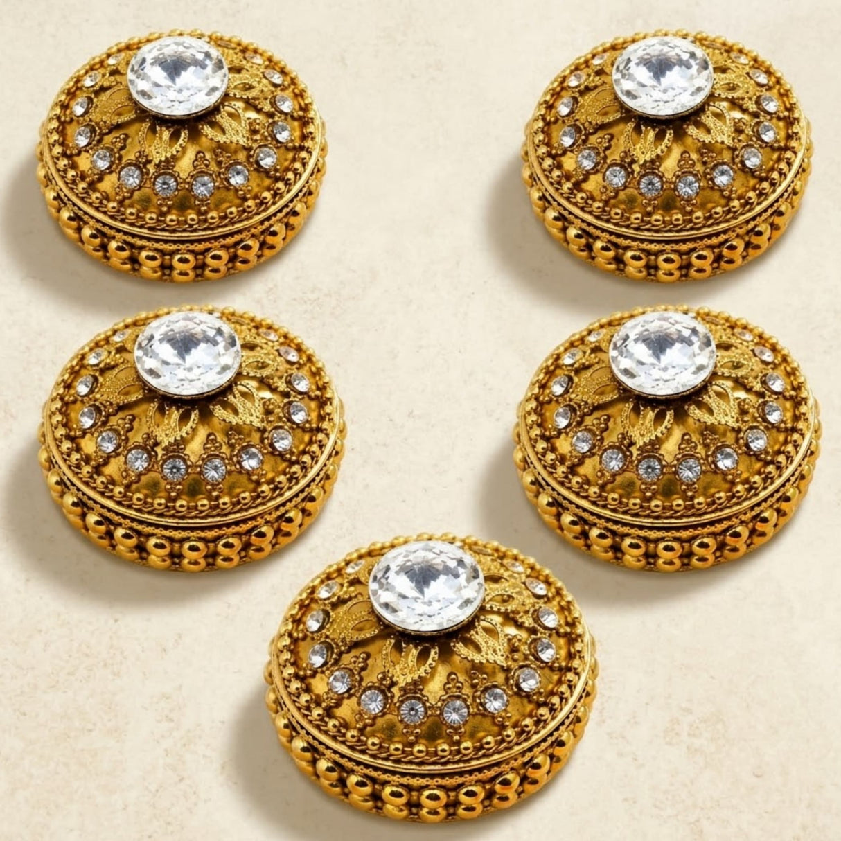 Gold-colored ornate button-like embellishments with intricate filigree and central clear crystal on golden kumkum holder