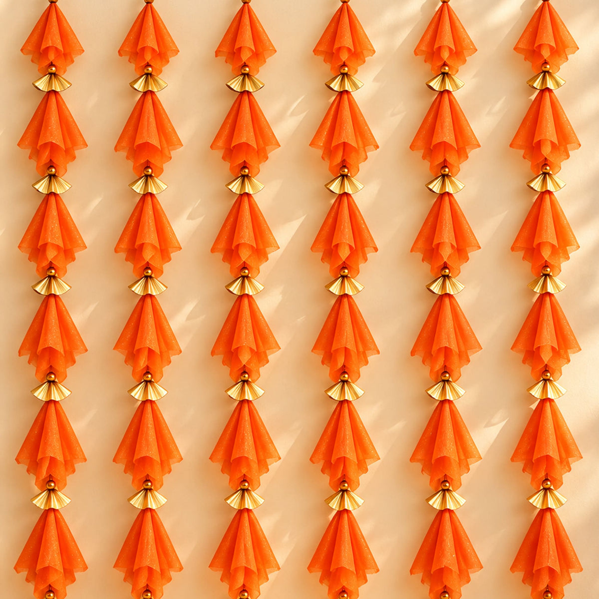 Orange sheer fabric tassels with gold metallic connectors on gotta patti net backdrop for diwali eid and wedding decor