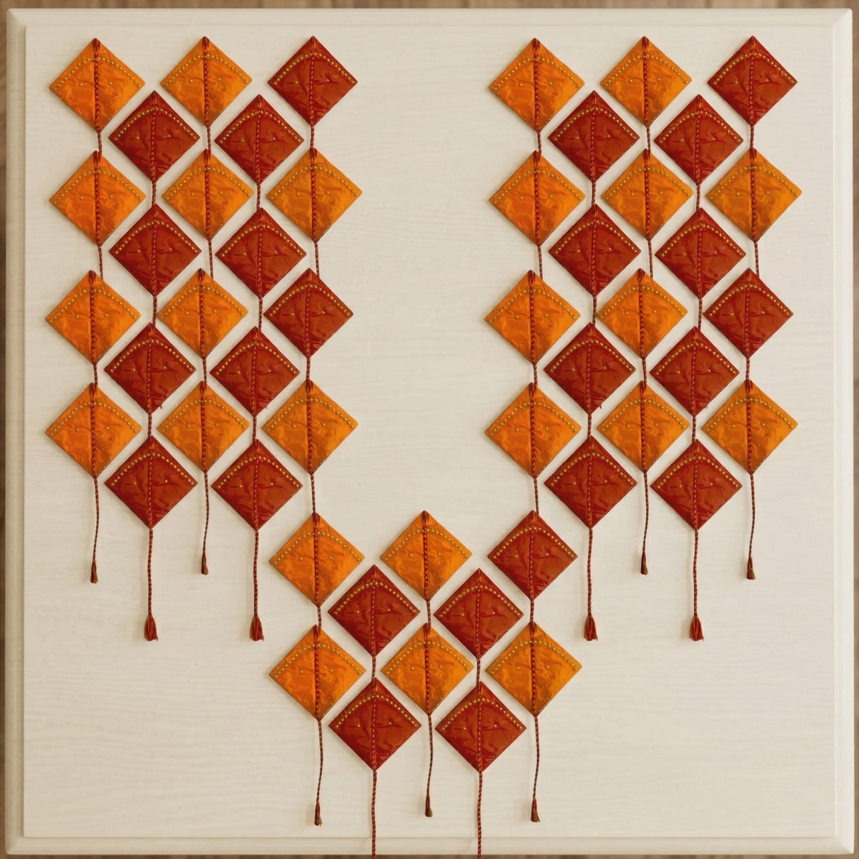 A vibrant orange and rust-colored quilted diamond wall art with stitched details and tassels for hindu festive decor