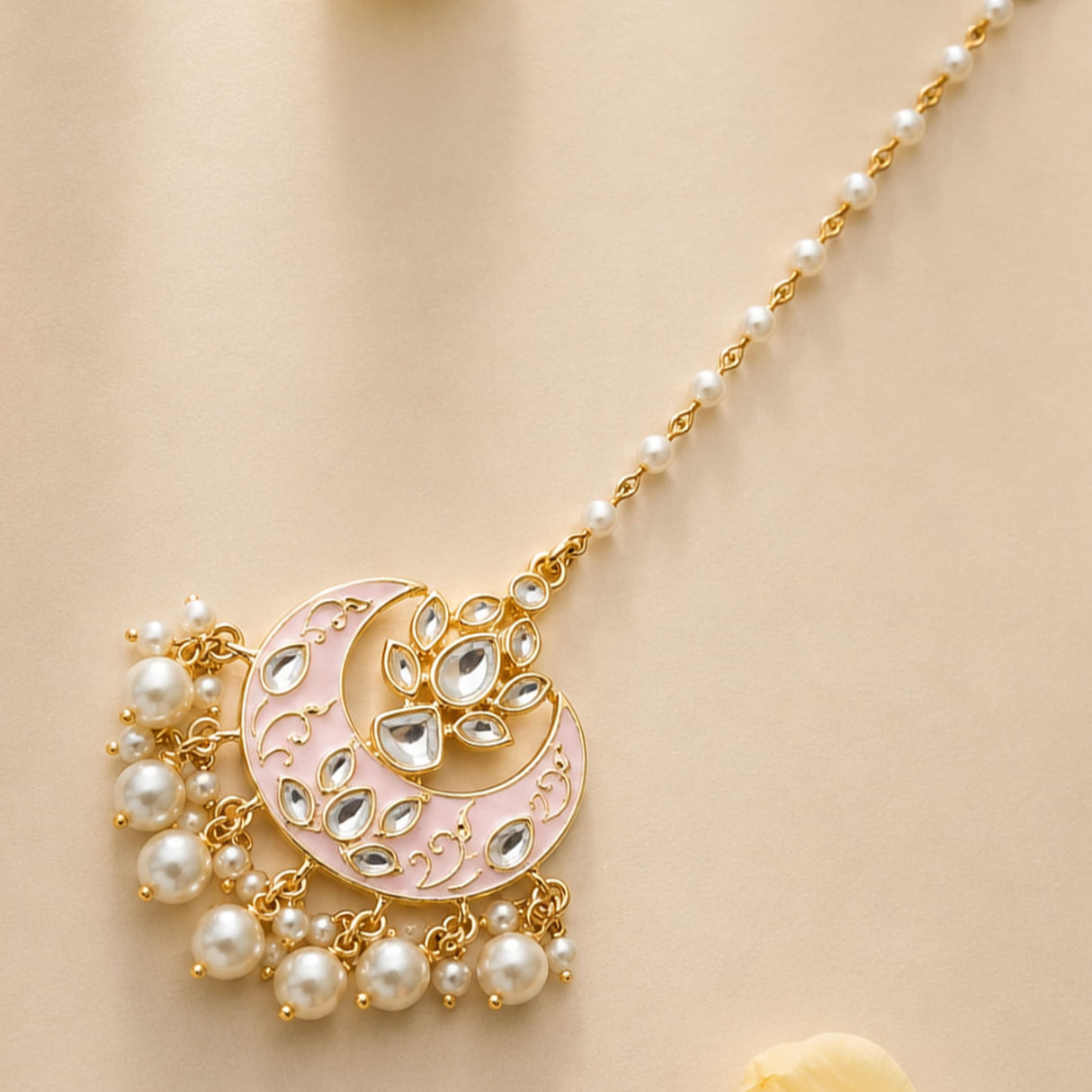 A gold-toned crescent-shaped kundan chand tikka with pink enamel clear stones and dangling white pearls for Indian weddings
