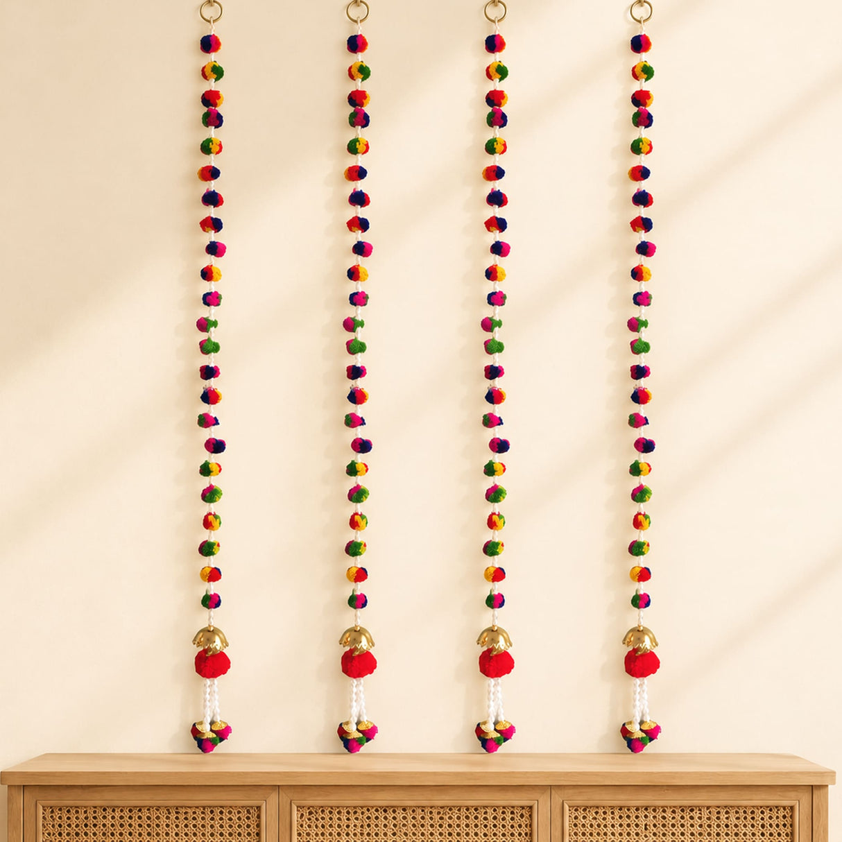 Four colorful pompoms wall hanging decorations with gold rings red pompoms and bells for diwali and indian weddings