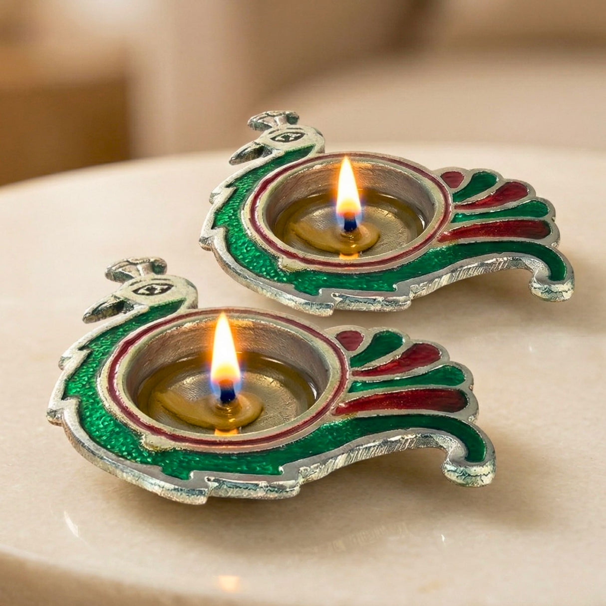 Two ornate peacock-shaped brass finish diya lamps with silver base and green red enamel for Diwali Puja decor
