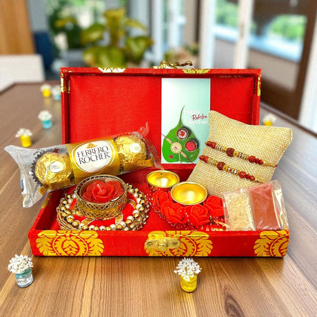 Red and gold Rakhi gift box with chocolates, candle holder, Haldi Kumkum, and Roli Chawal for Rakshabandhan