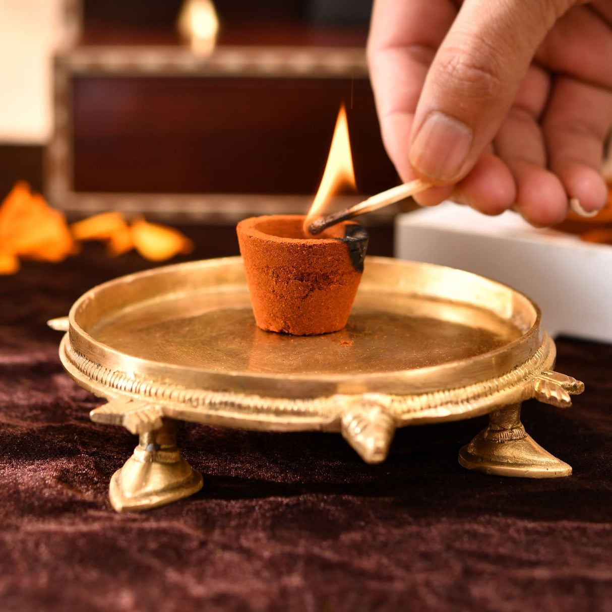 Hand holding lit terracotta clay diya above saffron sandalwood dhoop cups