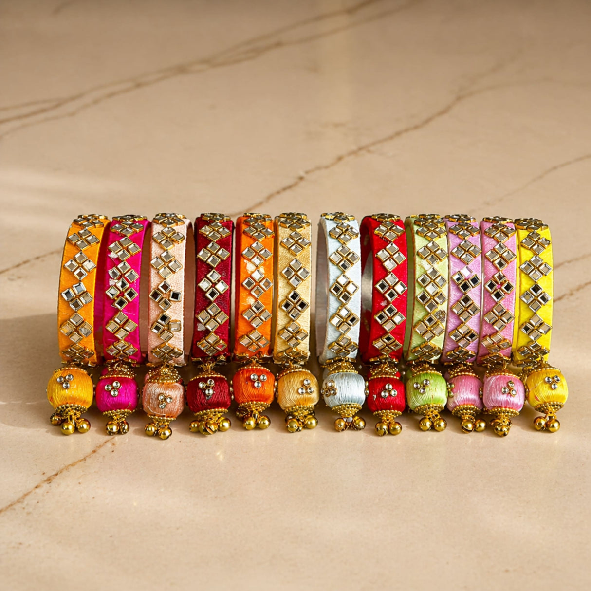 A vibrant array of silk thread bangles in orange pink red and yellow with gold-tone kundan embellishments and latkan tassels