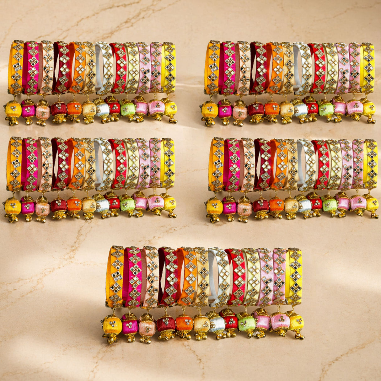 A collection of vibrant silk thread bangles in pink yellow orange and red with gold kundan embellishments and jingle bells