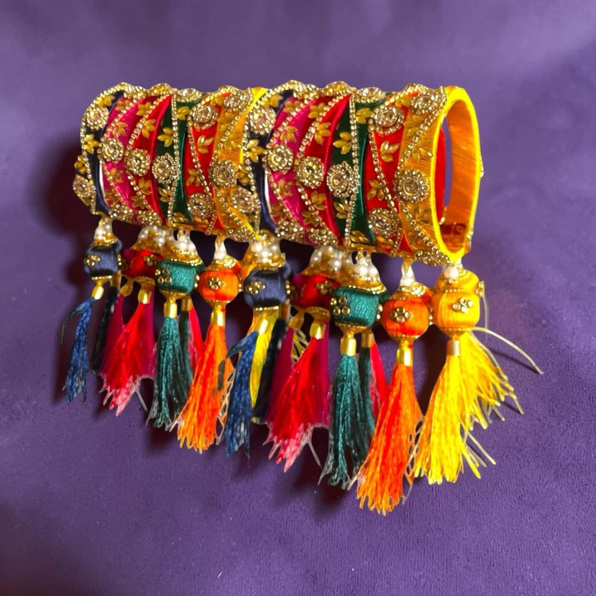 A set of vibrant silk thread bangles for women in pink red and yellow with kundan-style work and colorful tassels for festivals