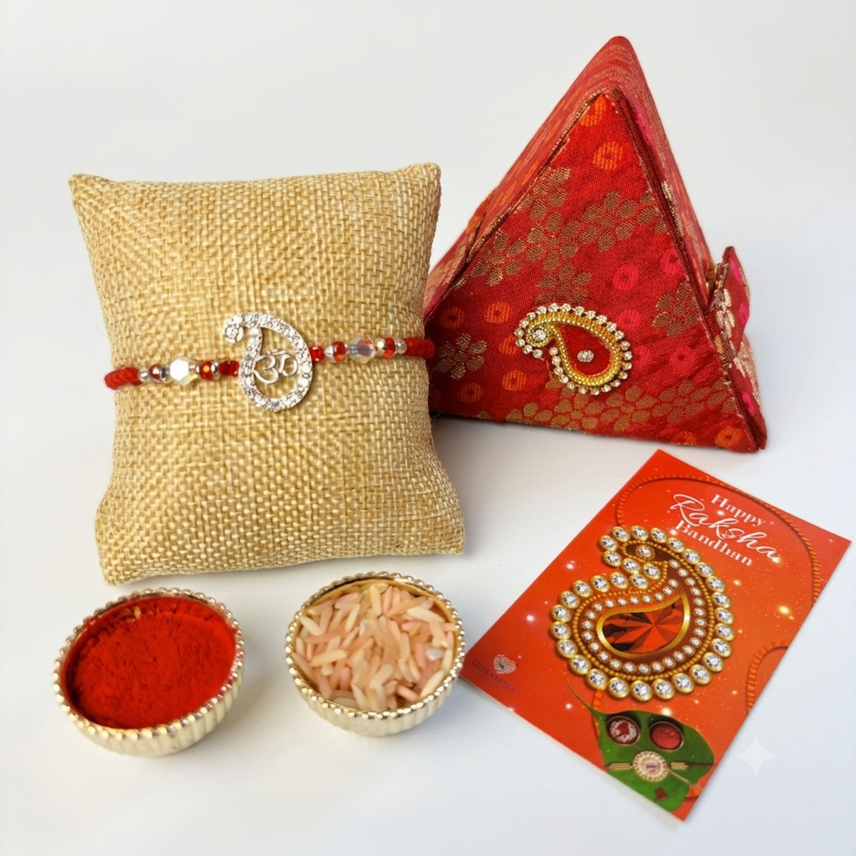 Red beaded designer pure silver om rakhi with diamond accents displayed on textured burlap cushion for Raksha Bandhan
