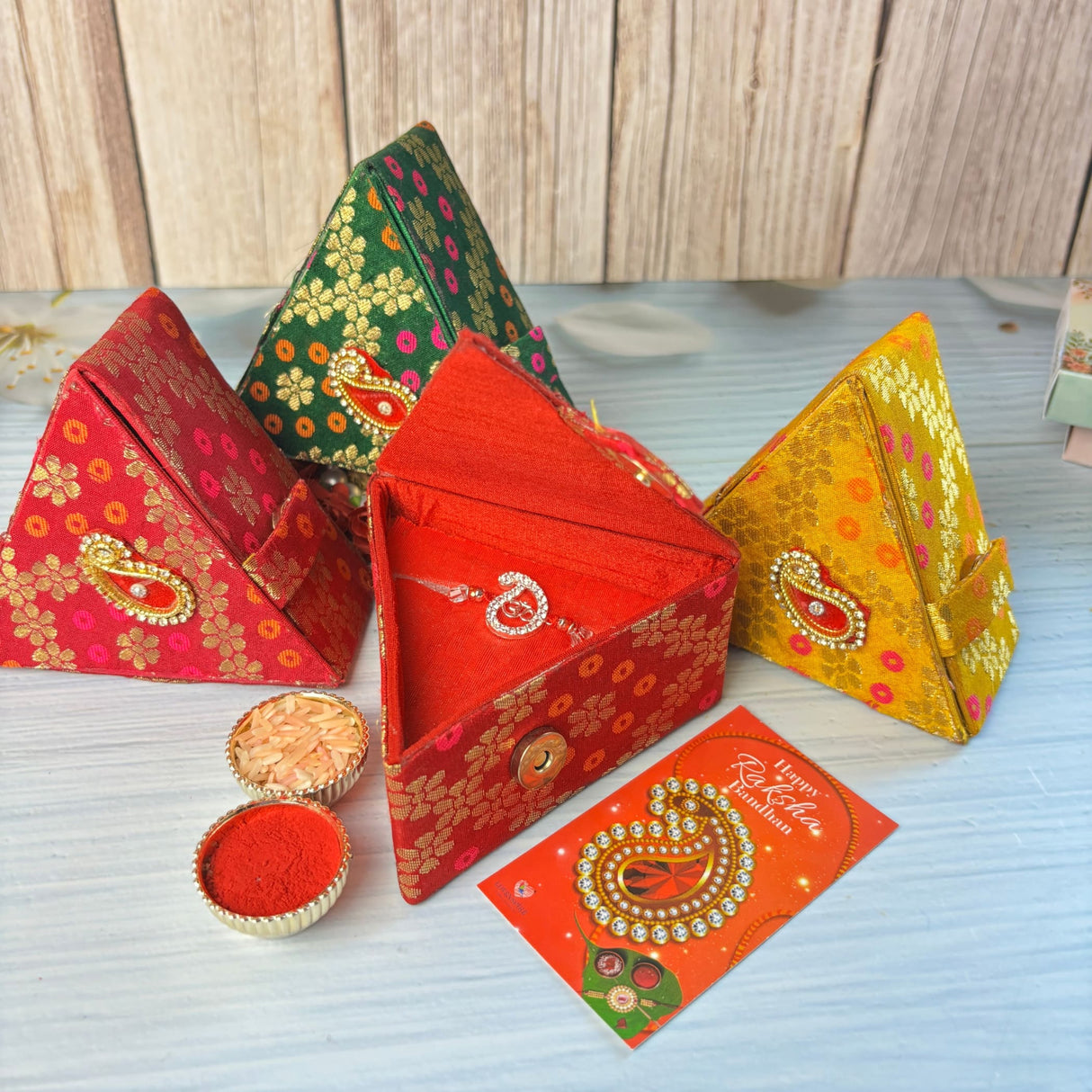 Red triangular brocade box with gold floral pattern and paisley clasp for designer pure silver om rakhi gift set