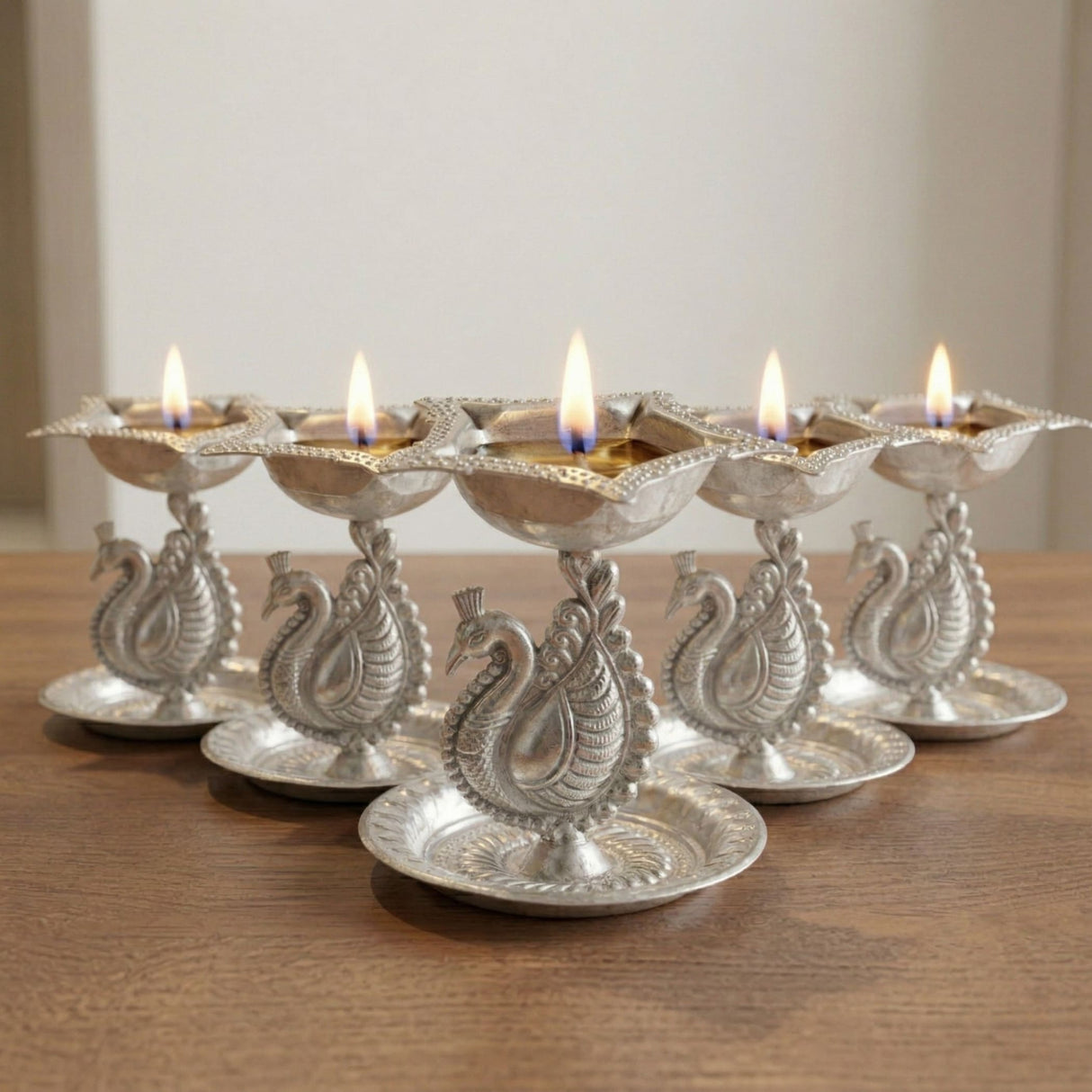 Silver plated peacock diya oil lamp with intricate engravings and lit candles for home pooja mandir and diwali decor
