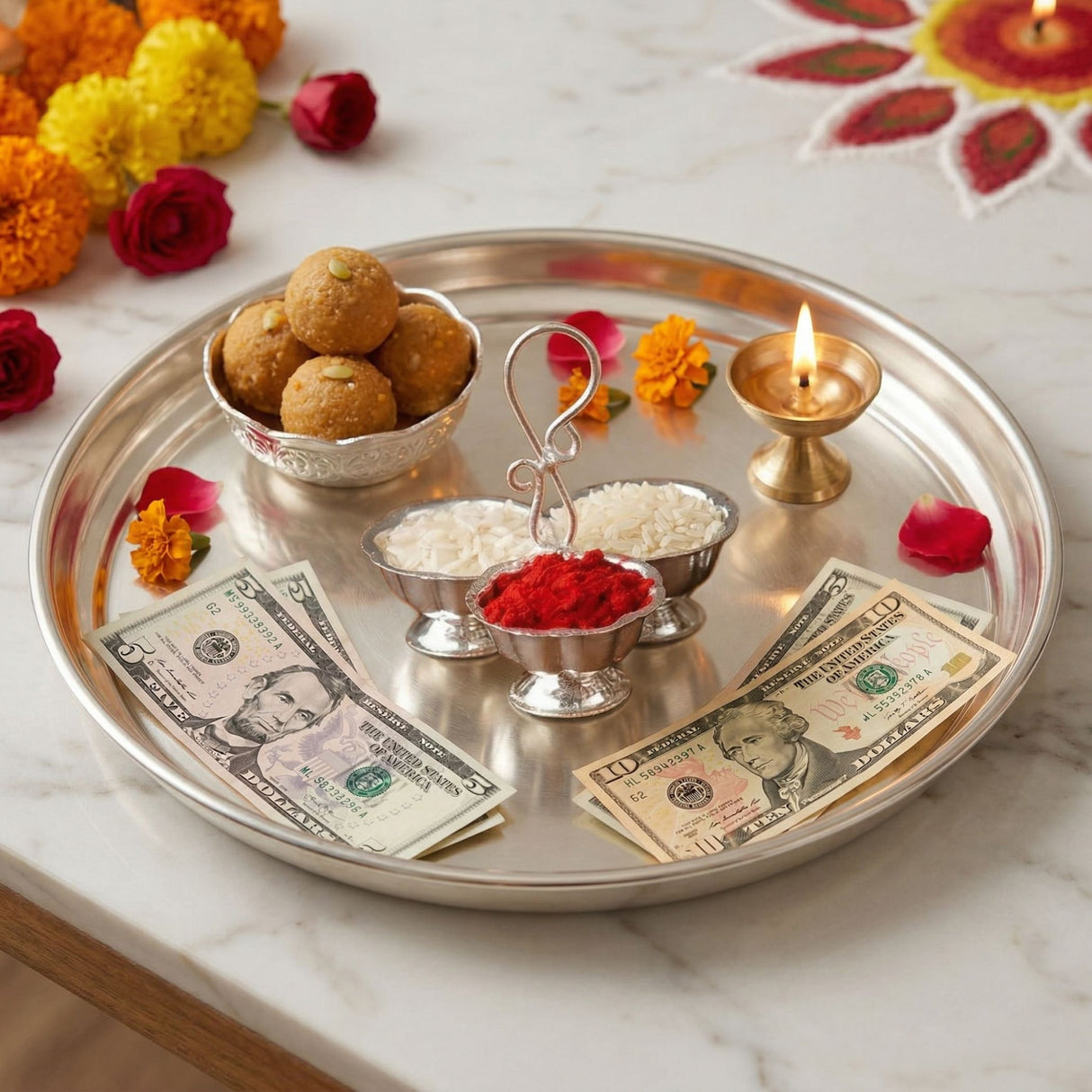 Silver plated round haldi kumkum tray with ornate edges holding laddoos bowls of rice red powder sugar diya for puja