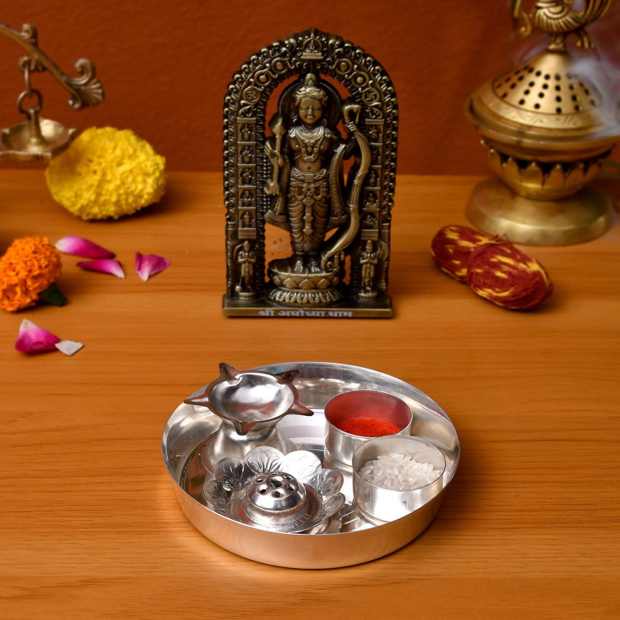 Silver plated pooja thali set with integrated compartments holding red powder white grains and decorative diya for rituals