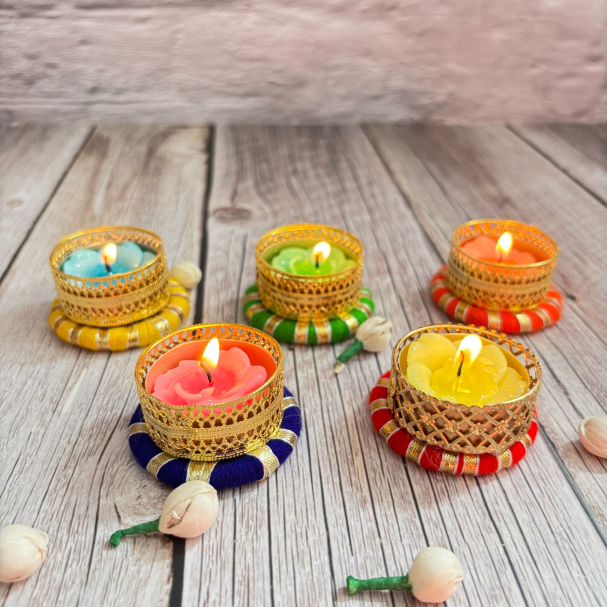 Colorful lit tea light candles in ornate golden holders on vibrant fabric bases for festive decor