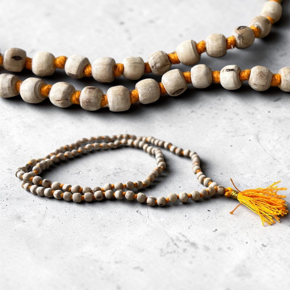 A handcrafted 5 mm tulsi mala beads necklace with light beige and orange wooden beads and a yellow tassel for meditation