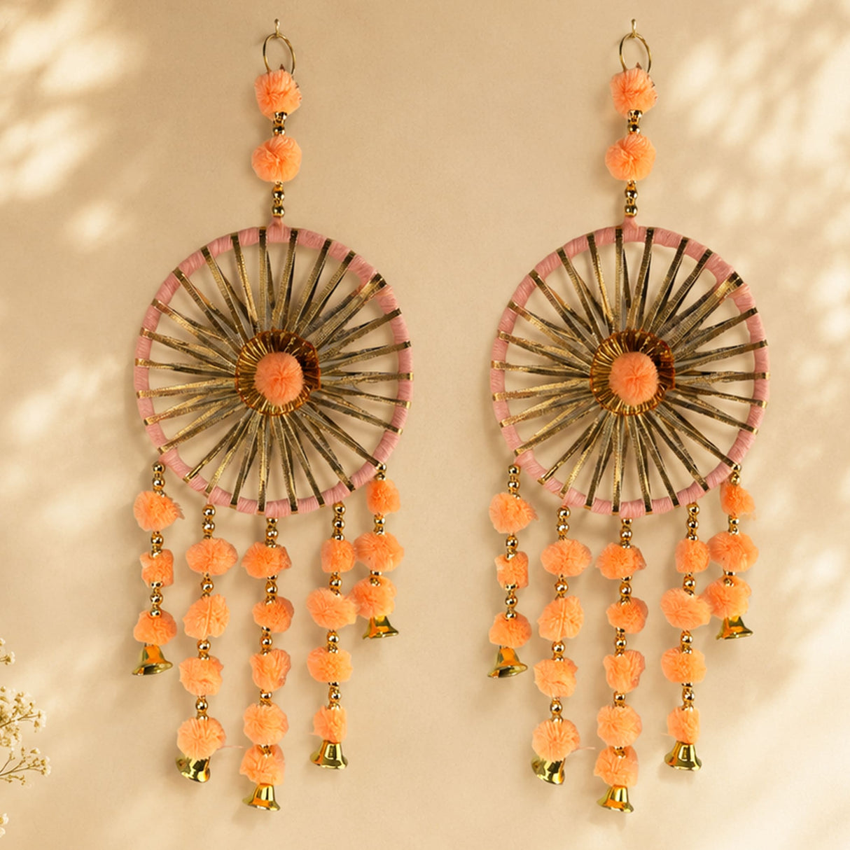 A pair of peach dreamcatcher earrings with gold frames pink trim and pom-poms in traditional Rajasthani style