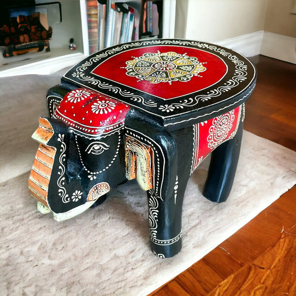 A black wooden elephant-shaped stool with red and white intricate traditional Indian designs.