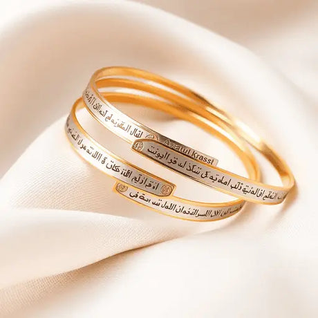 Close-up of elegant gold and silver bangles with intricate Ayatul Kursi inscriptions, artistically arranged on a soft fabric background, showcasing their craftsmanship and beauty.